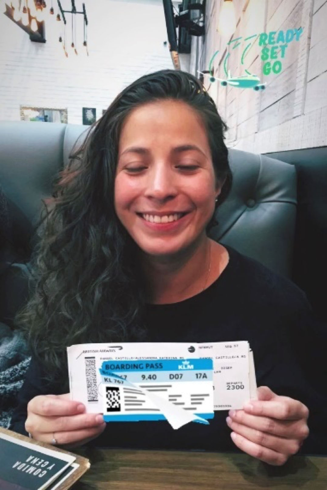 Student sitting in a black leather couch smiling and holding a flight boarding pass