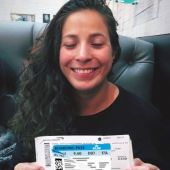 Student sitting in a black leather couch smiling and holding a flight boarding pass